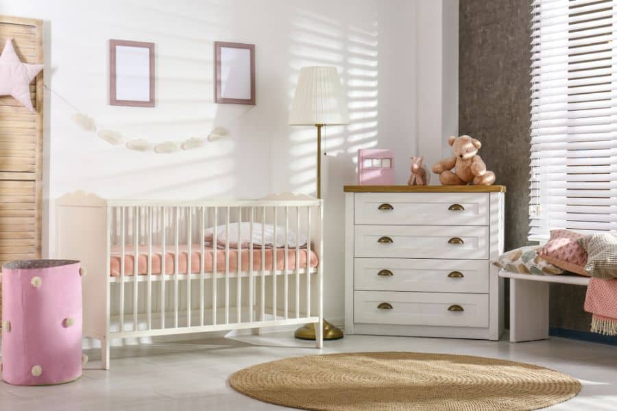 Bright baby girl's room with pink bedding, white crib, and soft natural lighting.