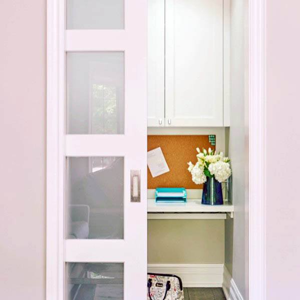 White pocket door with frosted glass panels opens to a small, organized workspace featuring white cabinets and fresh flowers