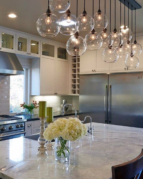 Modern kitchen with glass ball pendant lights hanging above a marble island, featuring stainless steel appliances and a bright, airy design