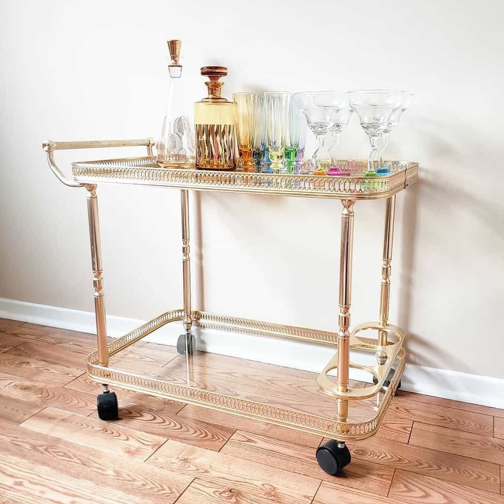 Elegant gold bar cart with glass decanters, colorful glassware, and martini glasses.