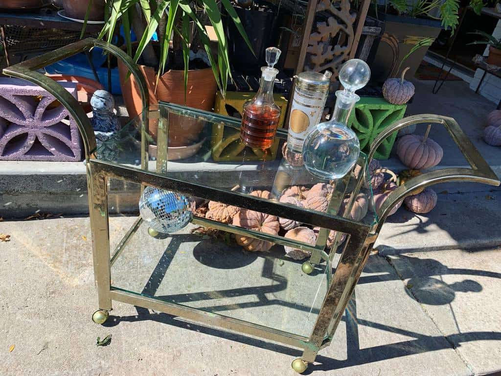 Gold bar cart with glass decanters, a disco ball, and outdoor decor.