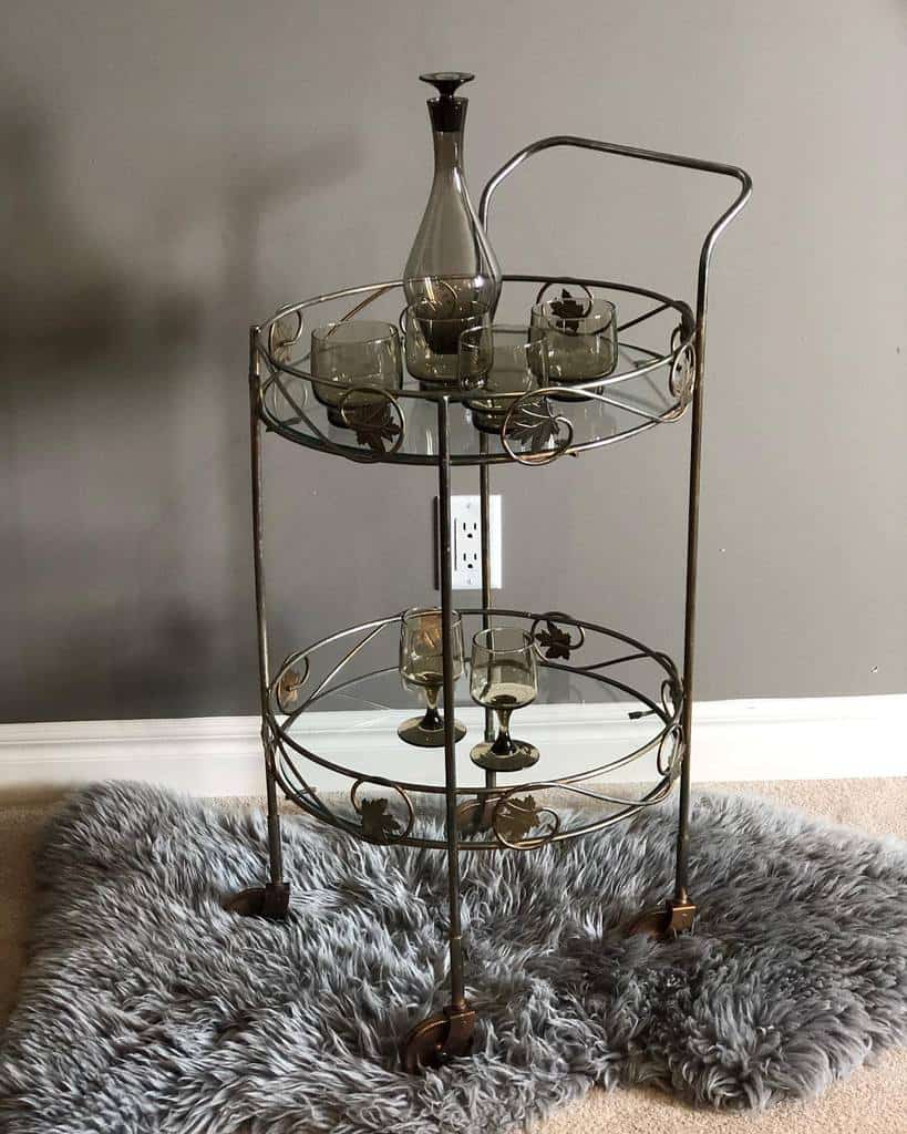 Vintage bar cart with glass decanter and matching tumblers on a faux fur rug.