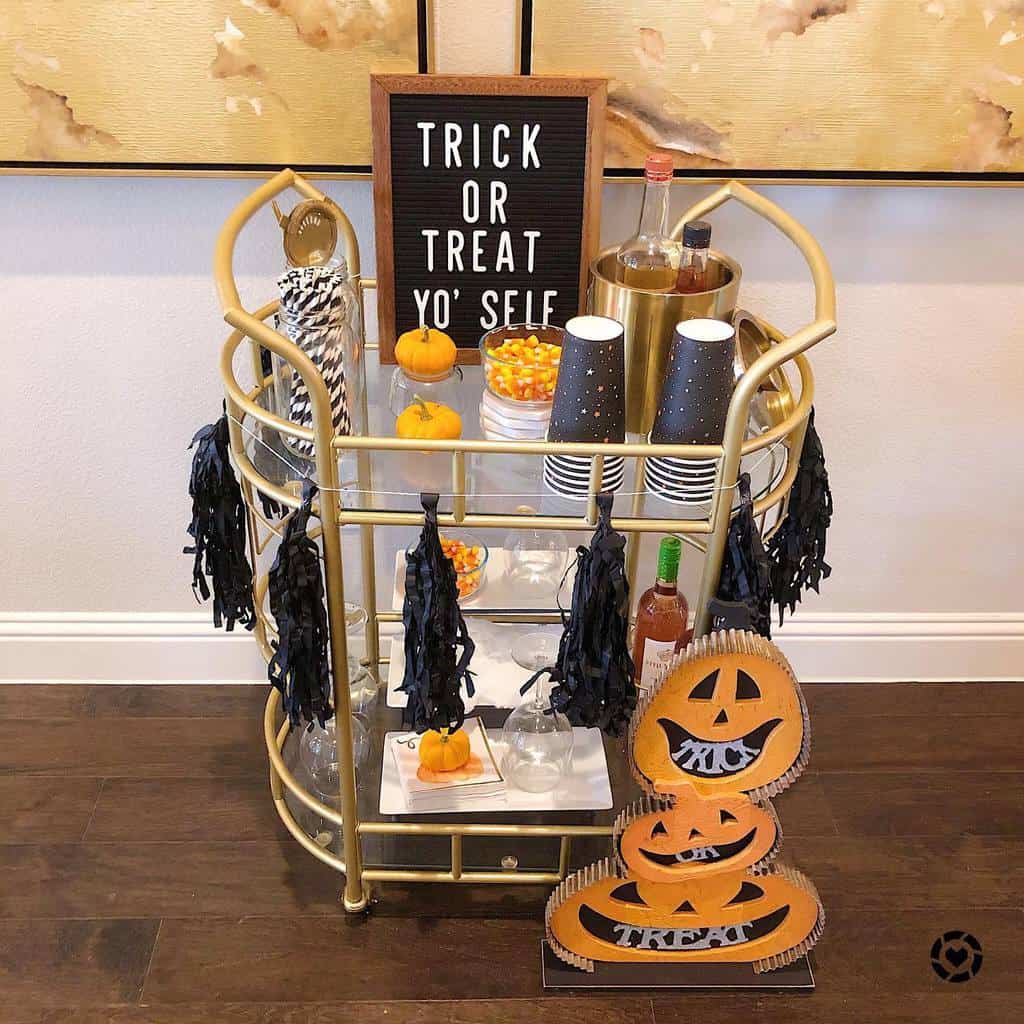 Halloween-themed bar cart with candy corn, mini pumpkins, black tassels, and festive decor.