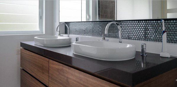 Bathroom with black mosaic tile backsplash, double vessel sinks, and wooden vanity.