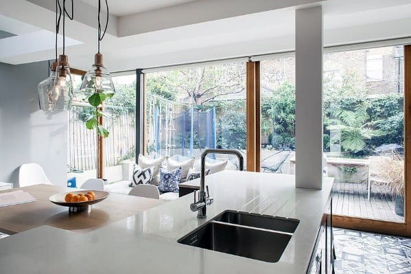 Charming kitchen with glass pendant lights above a white island, overlooking a garden through large windows with natural ligh