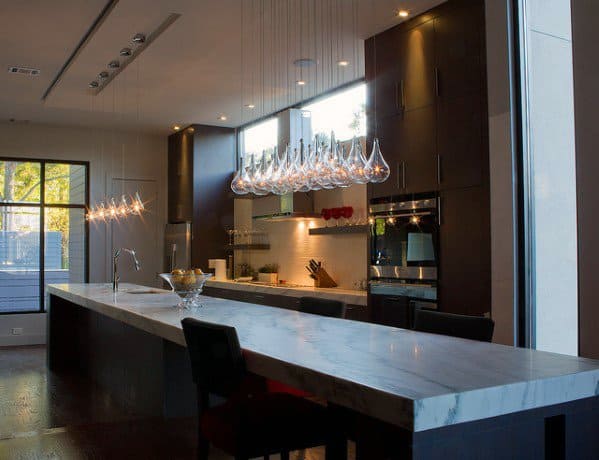 Modern kitchen with sleek glass pendant lights above a marble island, creating a sophisticated look with natural lighting