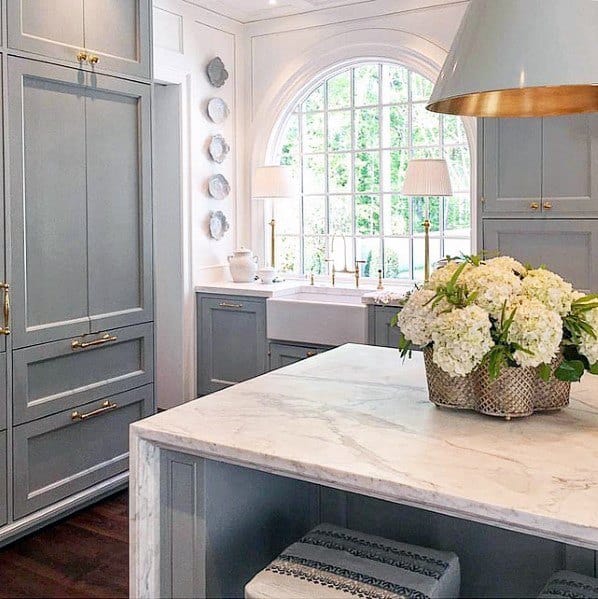 Elegant kitchen with a gold and grey large pendant lamp above a marble island, complemented by soft lighting and a spacious window