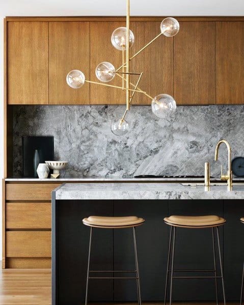 Stylish kitchen featuring a gold contemporary light fixture above a marble island, with wood cabinetry and modern bar stools