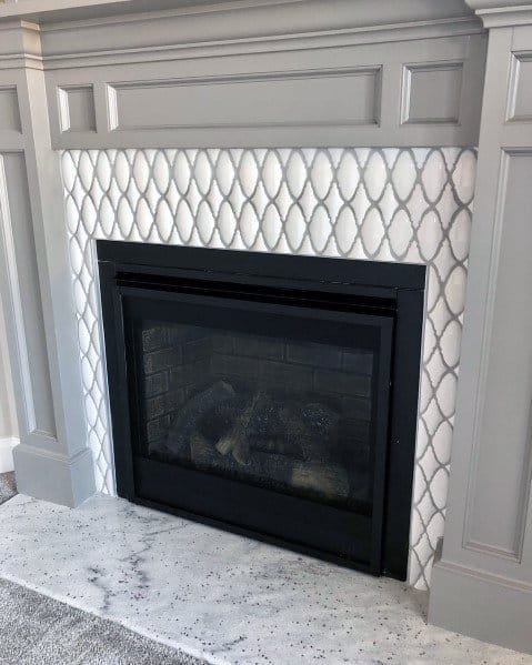 A sophisticated fireplace featuring elegant white lattice-patterned tiles, bordered by a soft gray mantle for a refined and polished look.