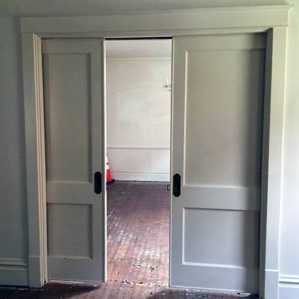 Classic double pocket doors with black handles open to an unfinished room, featuring neutral tones and wood flooring