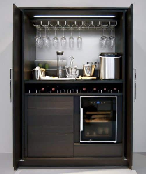 Modern mini bar with hanging glass rack, wine fridge, dark cabinets, and countertop accessories.