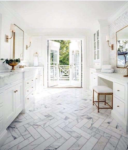 Spacious white bathroom with marble herringbone flooring, gold accents, and outdoor access.