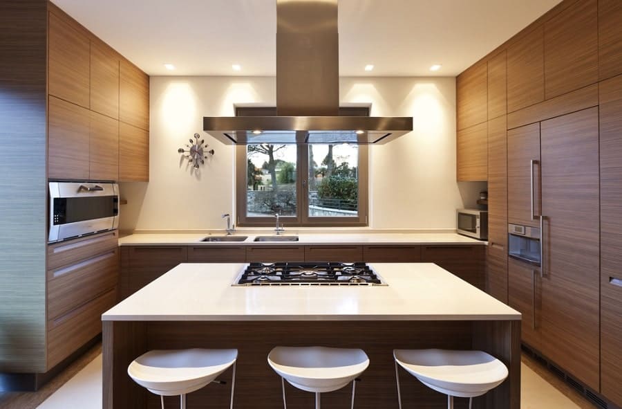 Modern kitchen with wood cabinets, island stove, extractor hood, stools, and a window view