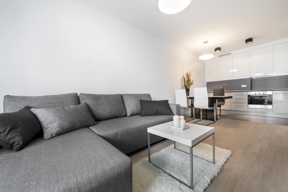 Minimalist open-plan living room with a gray sectional sofa, white coffee table, and modern kitchen in the background