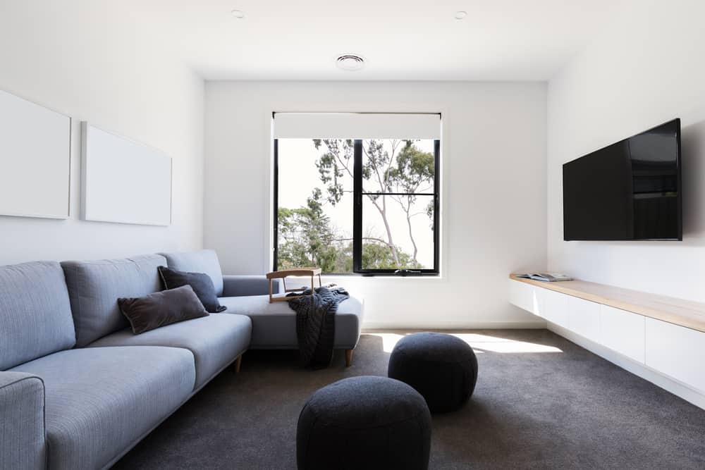 Minimalist living room with a light gray sofa, black ottomans, mounted TV, and a large window with serene outdoor views