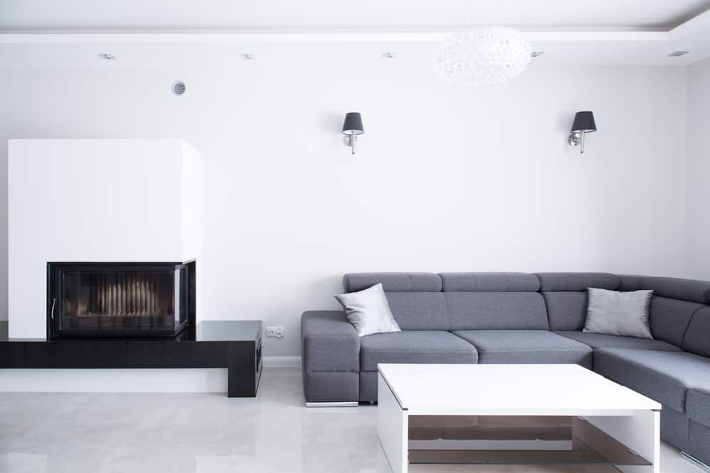 Minimalist living room with a gray sectional sofa, white coffee table, modern fireplace, and black wall sconces