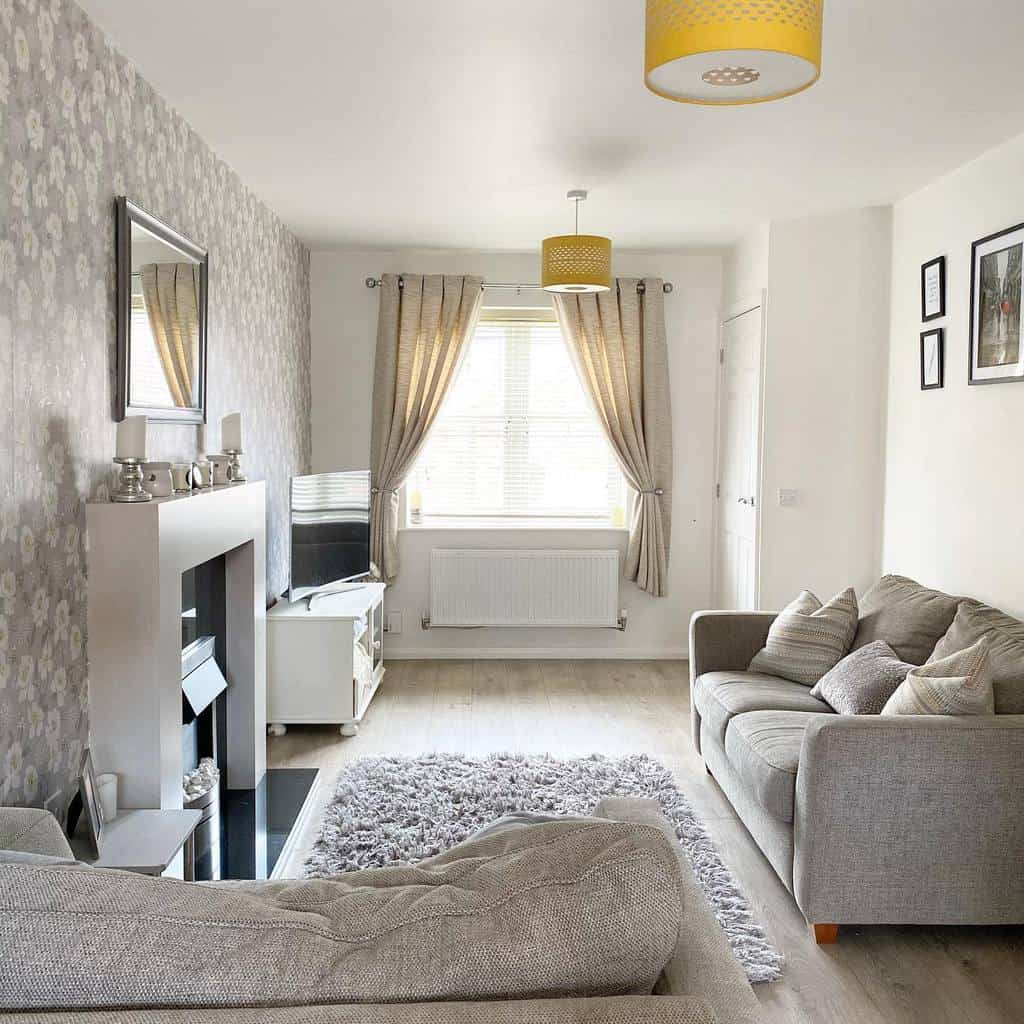 Cozy living room with gray sofas, floral wallpaper, a fireplace, and warm yellow accents creating a welcoming ambiance