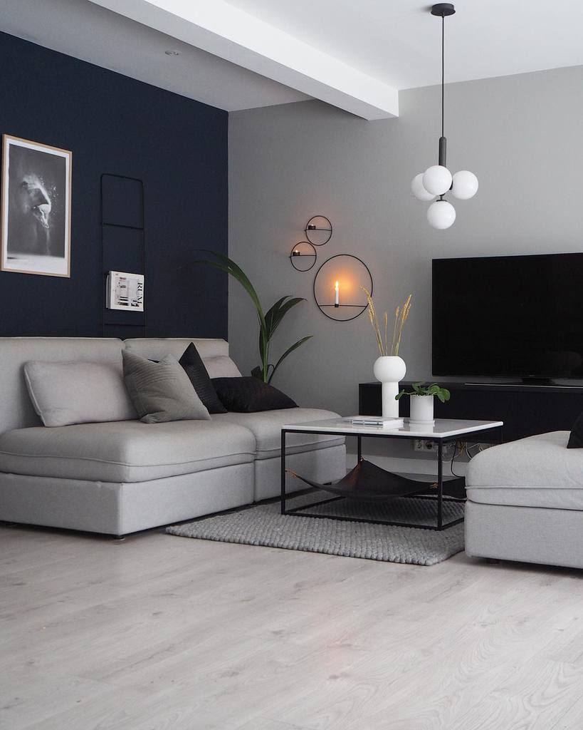 Modern living room with a gray sectional sofa, navy accent wall, geometric lighting, and minimalist decor