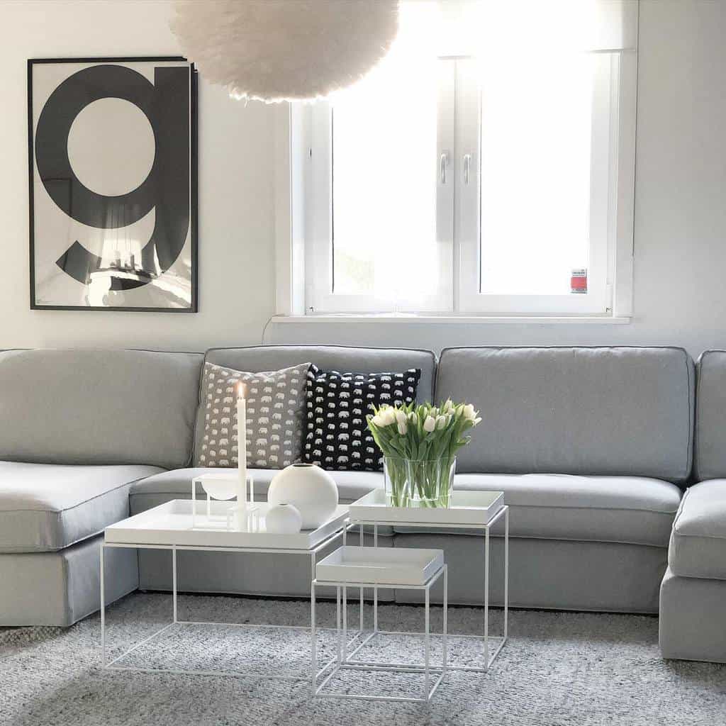 Bright living room with a gray sectional sofa, white nesting tables, modern wall art, and fresh tulips for decor