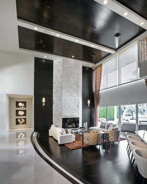 Modern living room with high ceilings, dark wood accents, white sofas, and large windows overlooking greenery