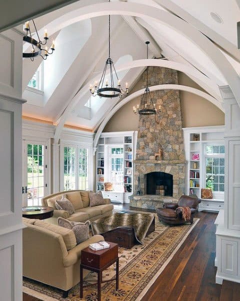 Cozy living room with vaulted ceiling, stone fireplace, elegant chandeliers, and plush seating on a patterned rug