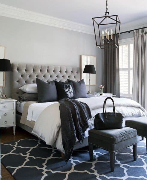 Elegant bedroom with tufted headboard, gray accents, and geometric rug under chandelier.