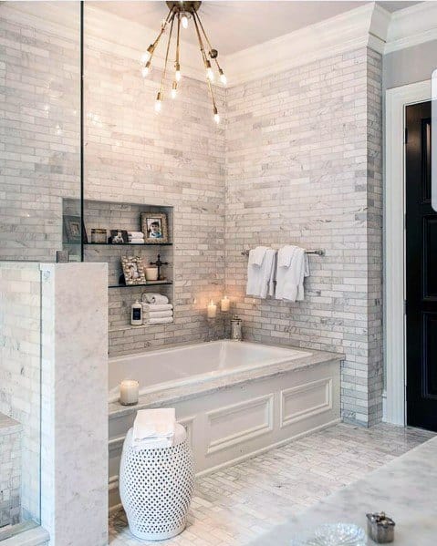 Luxurious bathroom with marble tile walls, built-in tub, and elegant lighting fixture.