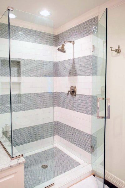 Glass shower with white and gray tiled walls, gray floor, and chrome fixtures