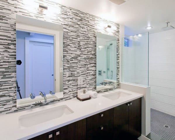 Bathroom with grey and white mosaic tile backsplash, double sinks, and glass shower.