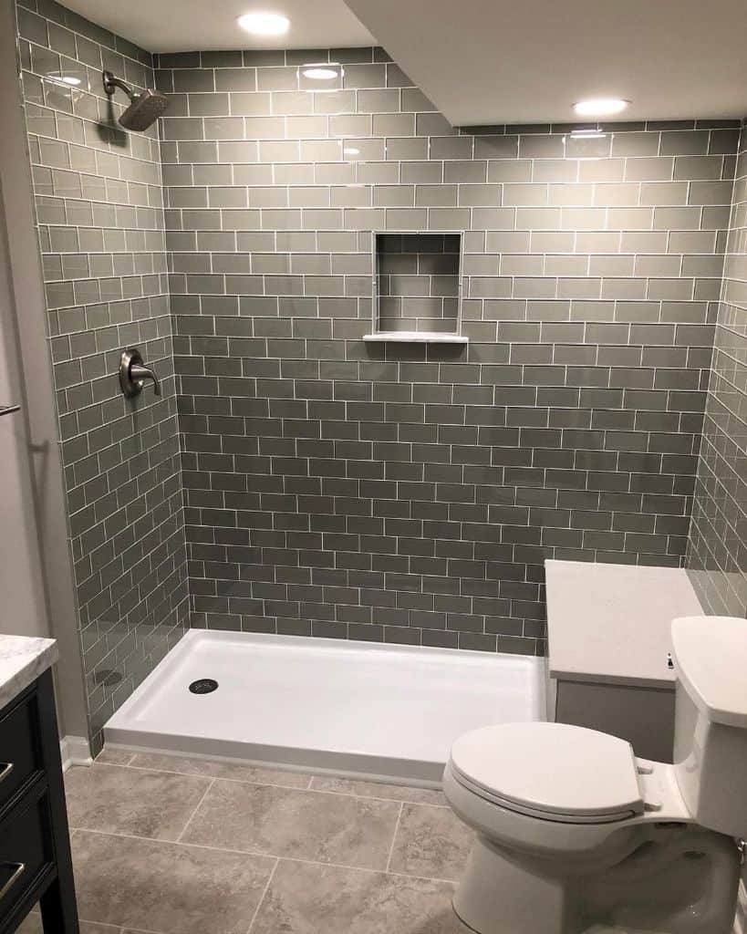 Basement bathroom with grey subway tiles, walk-in shower, and white toilet.