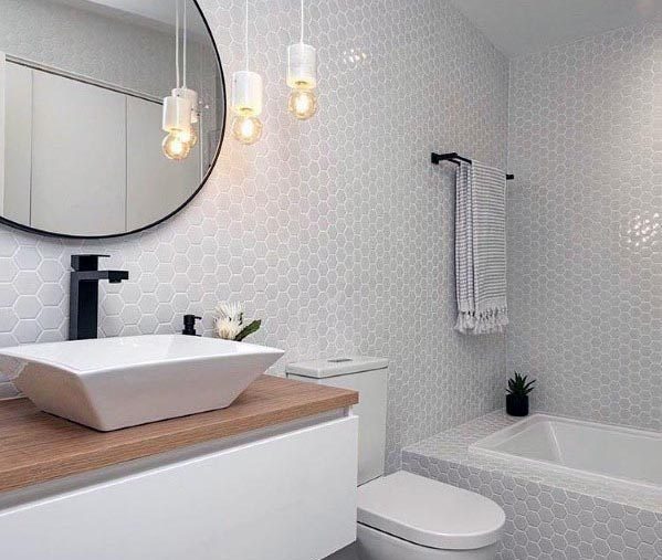 A chic grey bathroom with honeycomb tiles, a wooden vanity, a vessel sink, and modern pendant lighting.