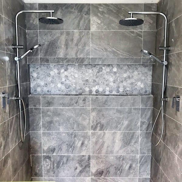 Dual showerheads with grey tiled walls and pebble accent in a modern bathroom