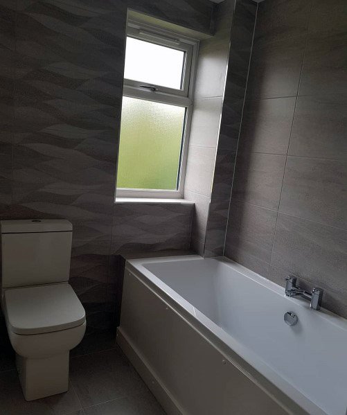 Grey-themed bathroom with a toilet, bathtub, and frosted window