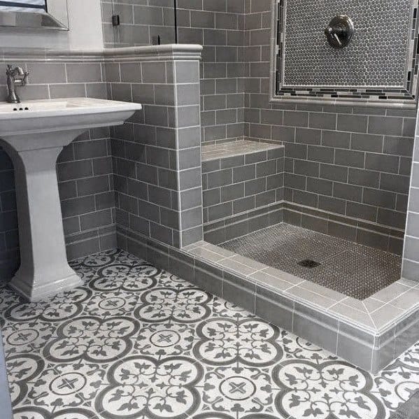 Bathroom with grey tiles, decorative floor, pedestal sink, and a step-in shower