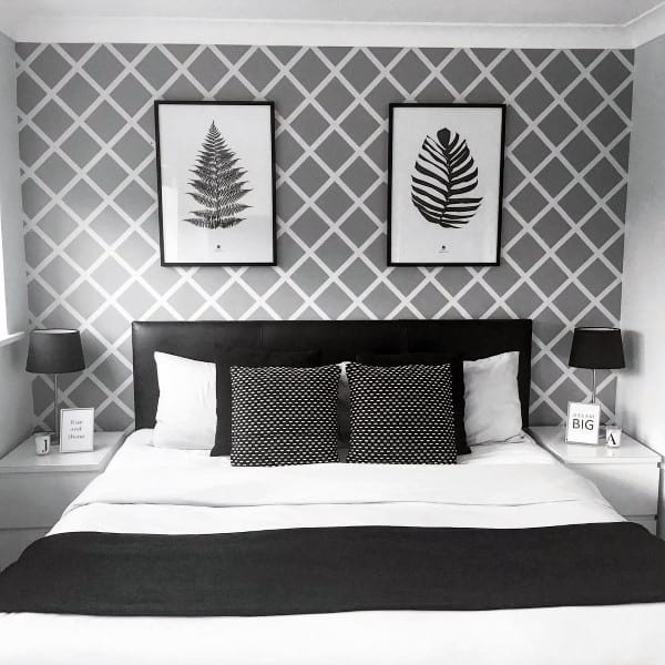 Modern bedroom with geometric wallpaper, framed fern prints, and monochrome bedding; minimalist decor on side tables