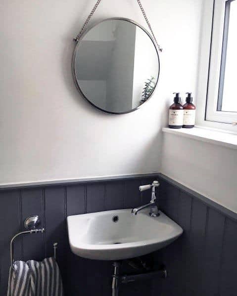 Compact bathroom with a white basin, dark grey wainscoting, and a round hanging mirror.