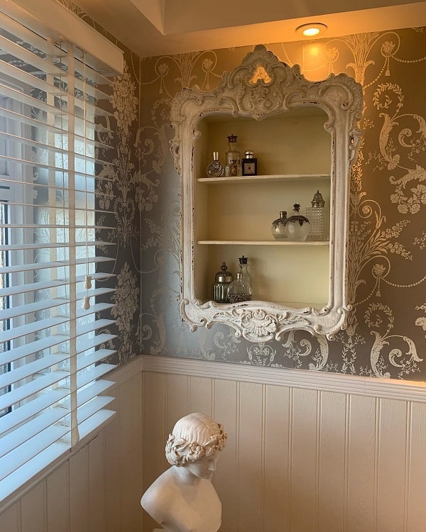 French-style bathroom with ornate mirror shelf, floral wallpaper, and bust statue decor.