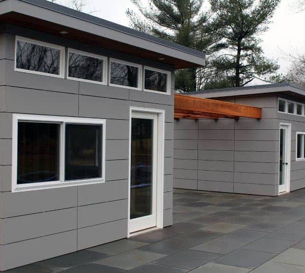 Modern gray pre-fabricated vinyl shed with large windows and a flat roof, connected by a patio.