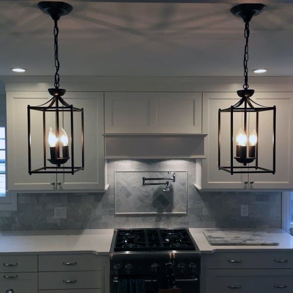 White kitchen with black lantern pendant lights marble backsplash and stainless steel stove.