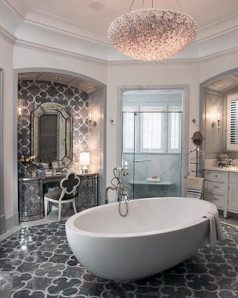 Luxurious master bathroom with white freestanding tub, patterned tile flooring, and crystal chandelier.