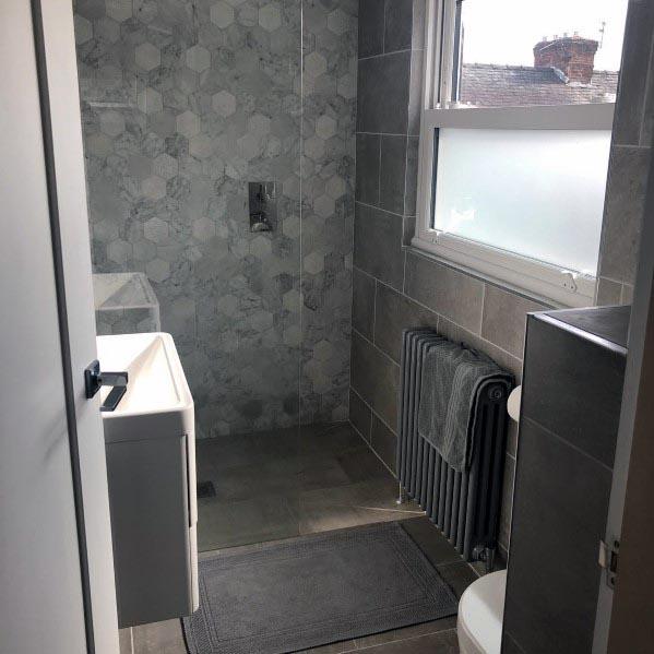 Compact bathroom with grey tiles, a hexagonal accent wall in the shower, and a frosted window.