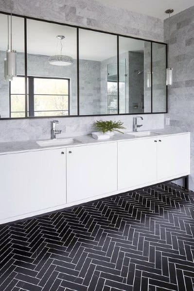 Elegant bathroom with grey wall tiles, large mirrors, and black herringbone floor tiles.