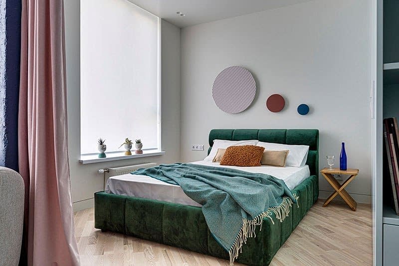 Modern bedroom with a plush green bed, cozy pillows, and a teal throw featuring minimalist decor on light-colored walls