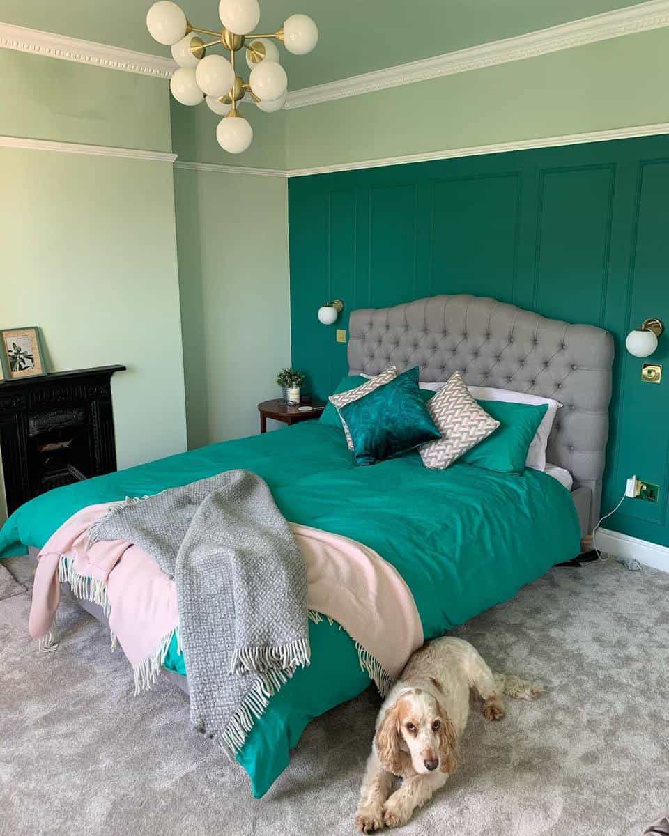 A cozy bedroom with a teal theme, a tufted headboard, and a dog lying on the carpet beside the bed