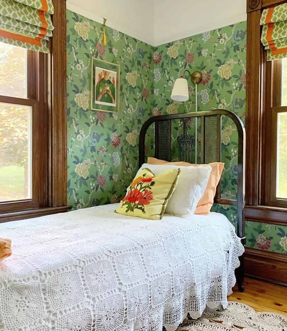 Cozy room with floral wallpaper, vintage bed, crocheted blanket, and decorative pillow near two windows