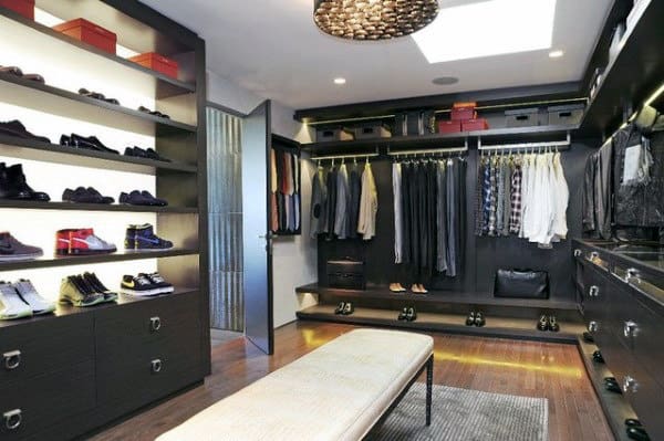 Spacious walk-in closet with shelves for shoes, hanging clothes, and storage boxes, and a central bench under ceiling light