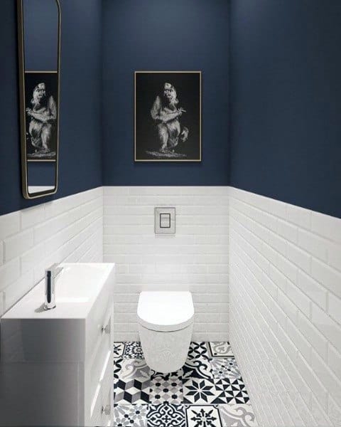 Stylish half bath with blue walls, decorative tiles, a white toilet, and a framed monkey art piece