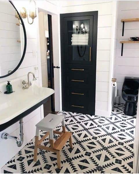 Modern farmhouse bathroom with shiplap walls, black cabinet, and geometric patterned floor tiles.