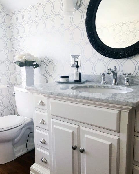 Bathroom with circular patterned wallpaper, white vanity, and black framed mirror.