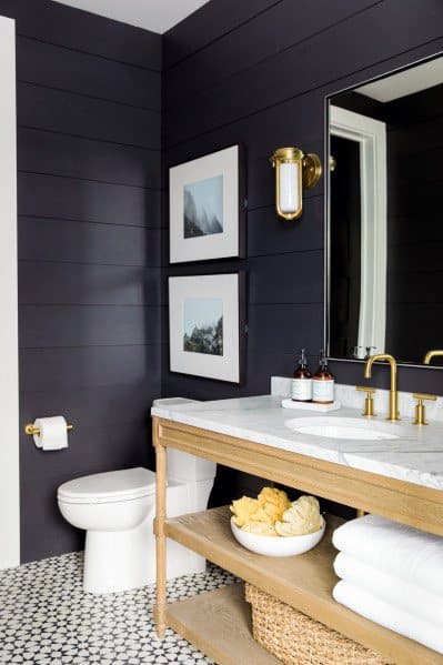 Country-style bathroom with black shiplap walls, wood vanity, and patterned tile flooring.